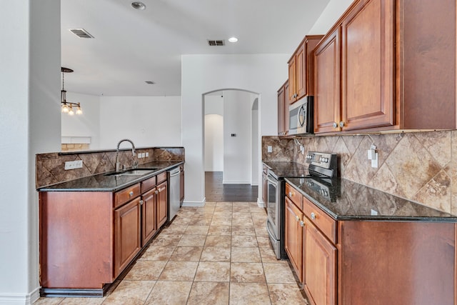 kitchen featuring appliances with stainless steel finishes, sink, backsplash, dark stone counters, and decorative light fixtures