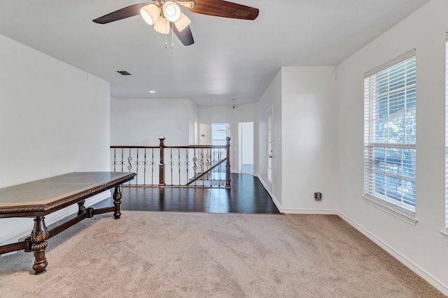 unfurnished room with a wealth of natural light, dark colored carpet, and ceiling fan