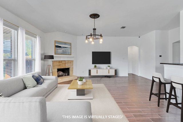 living room with a stone fireplace, wood-type flooring, and an inviting chandelier