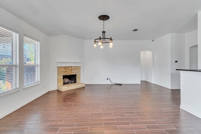 unfurnished living room with light hardwood / wood-style floors, a notable chandelier, and a stone fireplace