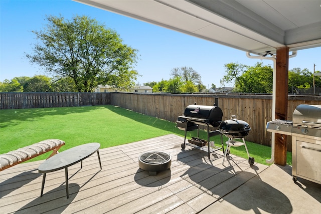 wooden terrace with a fire pit, a lawn, grilling area, and a fenced backyard