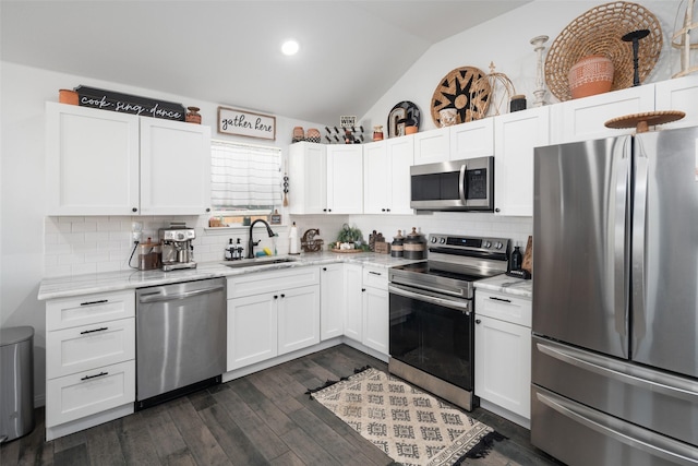 kitchen featuring light stone countertops, stainless steel appliances, lofted ceiling, white cabinetry, and a sink