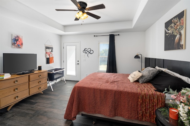 bedroom featuring a raised ceiling, dark wood-type flooring, and ceiling fan