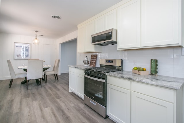 kitchen with decorative light fixtures, light wood-type flooring, white cabinetry, appliances with stainless steel finishes, and tasteful backsplash