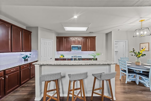 kitchen with a kitchen island with sink, an inviting chandelier, light stone counters, and appliances with stainless steel finishes