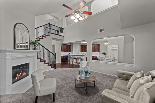 living room with dark colored carpet, ceiling fan with notable chandelier, and high vaulted ceiling