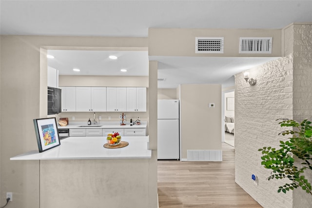 kitchen with kitchen peninsula, white cabinetry, light hardwood / wood-style flooring, white fridge, and sink