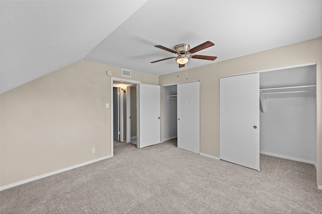 unfurnished bedroom with ceiling fan, light carpet, vaulted ceiling, and two closets