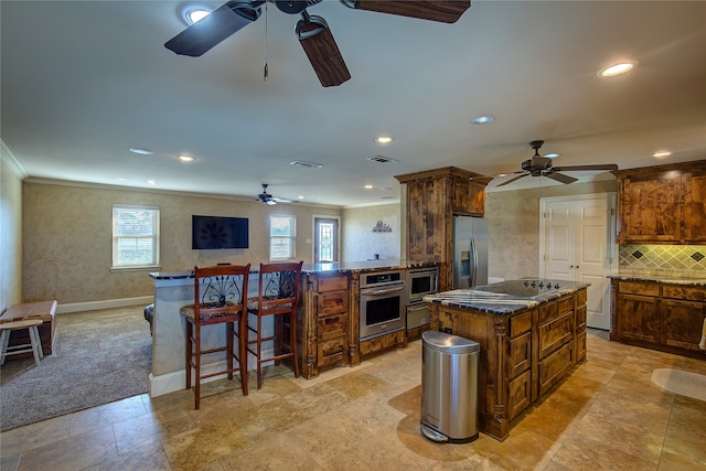 kitchen featuring a kitchen breakfast bar, backsplash, dark stone countertops, a center island, and appliances with stainless steel finishes