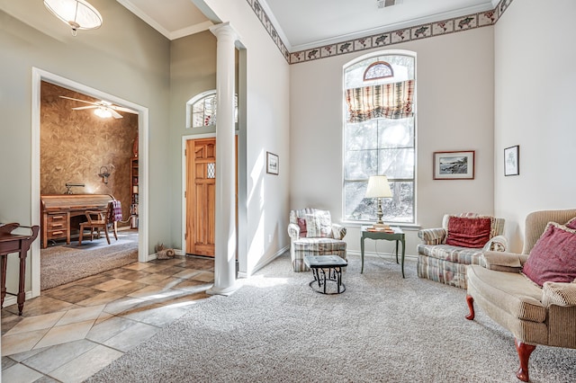 living area featuring ceiling fan, a towering ceiling, decorative columns, ornamental molding, and light carpet