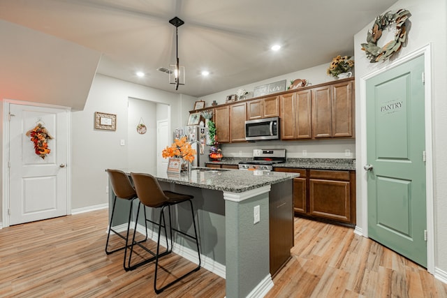 kitchen with dark stone countertops, pendant lighting, light hardwood / wood-style flooring, a kitchen island with sink, and appliances with stainless steel finishes