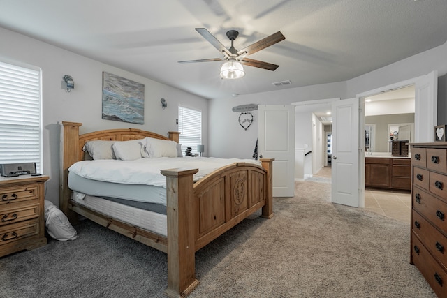 bedroom with ceiling fan, ensuite bath, and light carpet