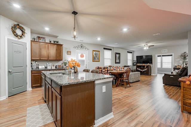 kitchen with decorative light fixtures, ceiling fan, light hardwood / wood-style floors, an island with sink, and light stone counters