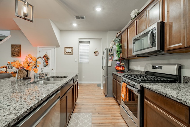 kitchen with sink, light stone counters, stainless steel appliances, and light hardwood / wood-style floors