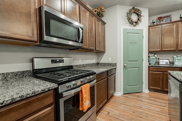 kitchen featuring appliances with stainless steel finishes, light hardwood / wood-style floors, and light stone counters