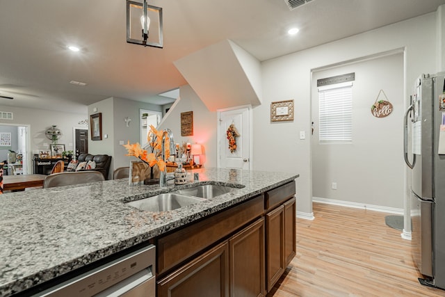 kitchen featuring light hardwood / wood-style floors, appliances with stainless steel finishes, decorative light fixtures, light stone counters, and sink