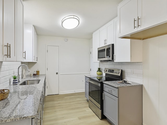 kitchen featuring appliances with stainless steel finishes, sink, white cabinetry, light stone counters, and light hardwood / wood-style flooring