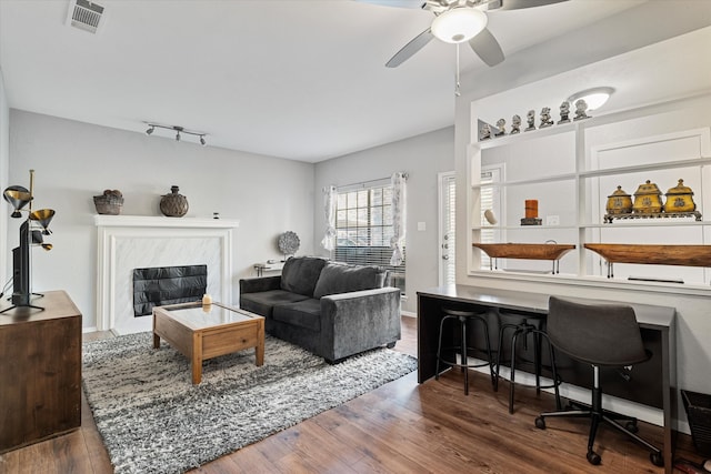 living room with a high end fireplace, ceiling fan, track lighting, and dark hardwood / wood-style flooring