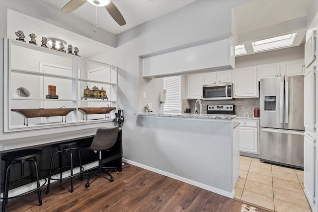 kitchen with kitchen peninsula, a breakfast bar, white cabinets, light wood-type flooring, and appliances with stainless steel finishes