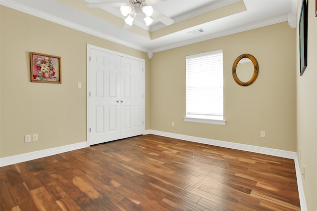 unfurnished bedroom featuring a tray ceiling, a closet, ceiling fan, crown molding, and hardwood / wood-style flooring