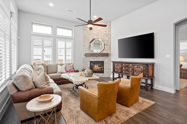 living room with ceiling fan, a stone fireplace, and dark hardwood / wood-style flooring