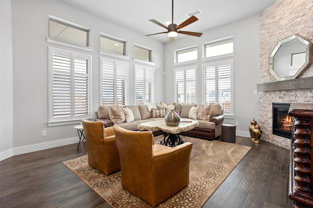 living room with ceiling fan, a stone fireplace, and dark hardwood / wood-style floors