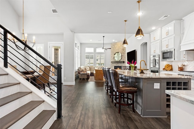 kitchen with hanging light fixtures, a kitchen breakfast bar, white cabinetry, light stone countertops, and a stone fireplace