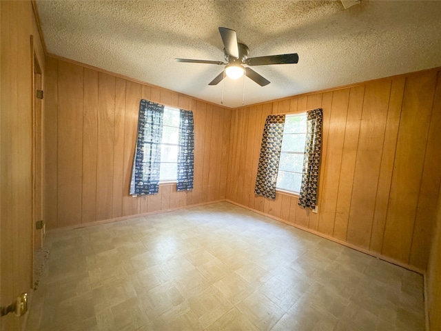 spare room featuring a wealth of natural light, ceiling fan, a textured ceiling, and wood walls