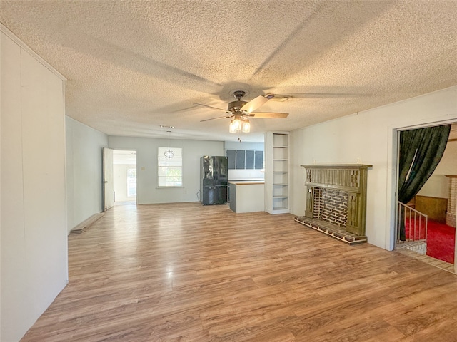 unfurnished living room with a textured ceiling, hardwood / wood-style flooring, ceiling fan, and a brick fireplace