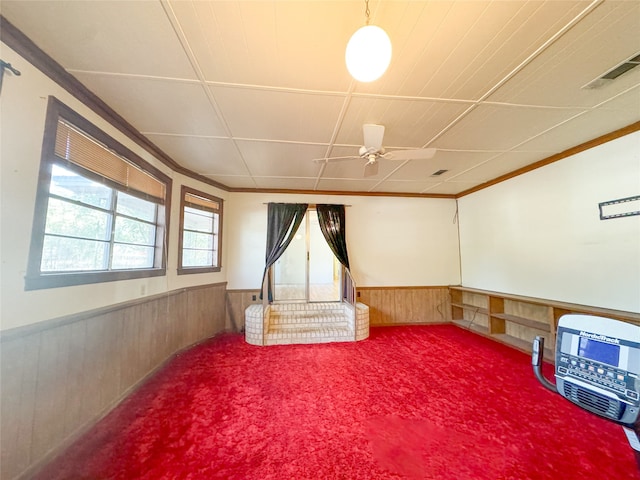 interior space with wooden walls, ornamental molding, carpet, heating unit, and ceiling fan