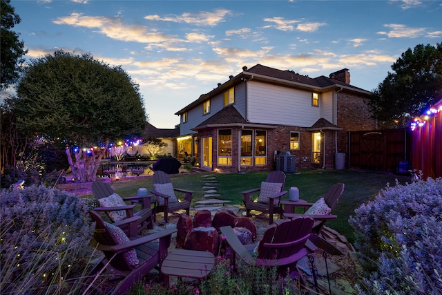 back house at dusk featuring a fire pit, cooling unit, and a lawn