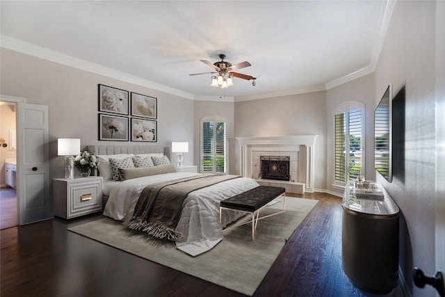 bedroom with ornamental molding, ceiling fan, a tile fireplace, connected bathroom, and dark hardwood / wood-style floors