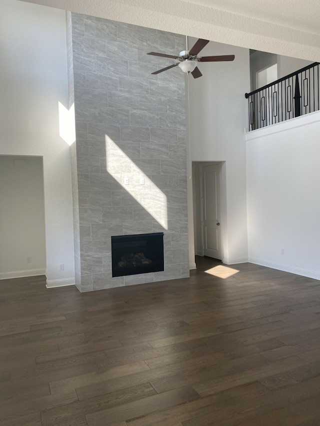 unfurnished living room with a high ceiling, ceiling fan, a tiled fireplace, and dark hardwood / wood-style flooring