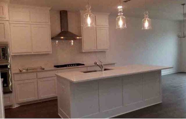 kitchen featuring oven, an island with sink, pendant lighting, wall chimney exhaust hood, and sink