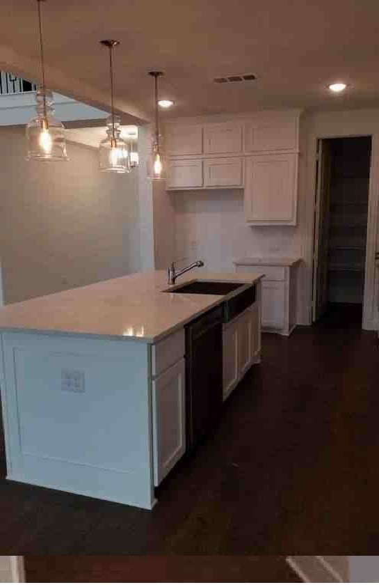 kitchen with a kitchen island with sink, sink, white cabinets, and decorative light fixtures