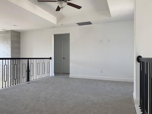 carpeted spare room with a tray ceiling and ceiling fan