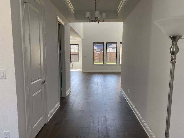 hall with crown molding, dark hardwood / wood-style floors, a chandelier, and a raised ceiling