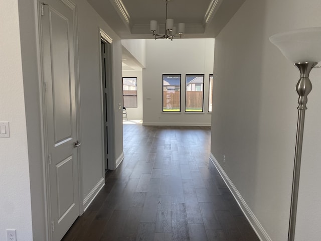 corridor with crown molding, a notable chandelier, dark hardwood / wood-style floors, and a raised ceiling