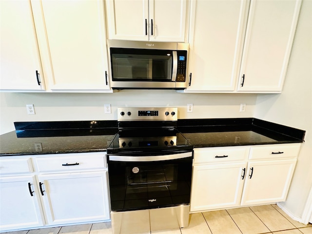 kitchen featuring white cabinets, stainless steel appliances, light tile patterned flooring, and dark stone countertops