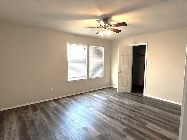 unfurnished bedroom featuring a spacious closet, dark wood-type flooring, ceiling fan, and a closet