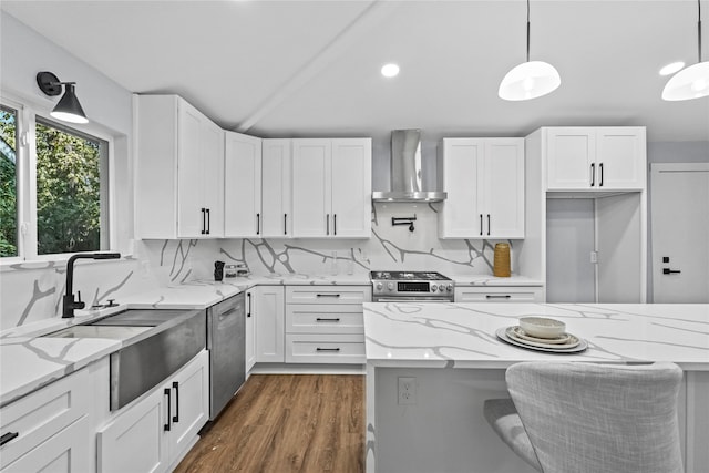 kitchen with white cabinetry, wall chimney exhaust hood, appliances with stainless steel finishes, and hanging light fixtures