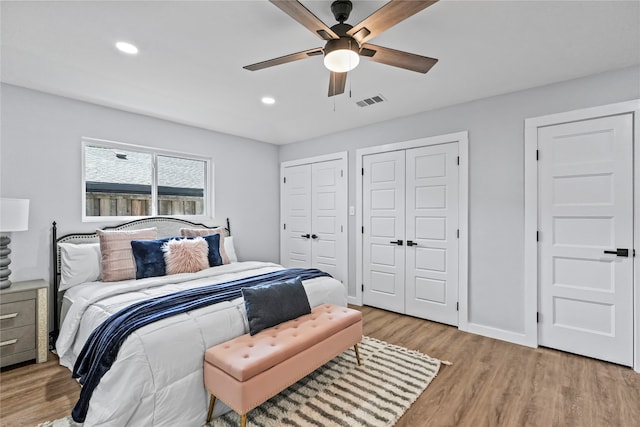 bedroom with light hardwood / wood-style floors, two closets, and ceiling fan