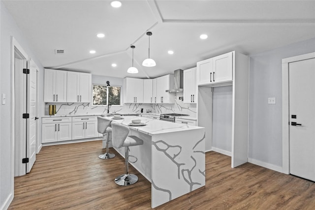 kitchen featuring wall chimney exhaust hood, dark wood-type flooring, a center island, white cabinetry, and light stone counters