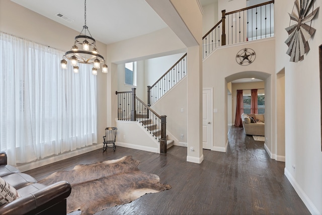 foyer entrance with dark wood-type flooring, a wealth of natural light, an inviting chandelier, and a high ceiling