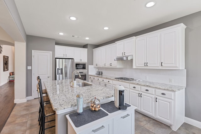 kitchen with stainless steel appliances, white cabinetry, and an island with sink