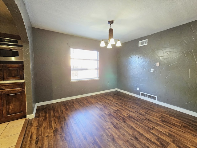 unfurnished dining area featuring hardwood / wood-style floors, a textured ceiling, and an inviting chandelier