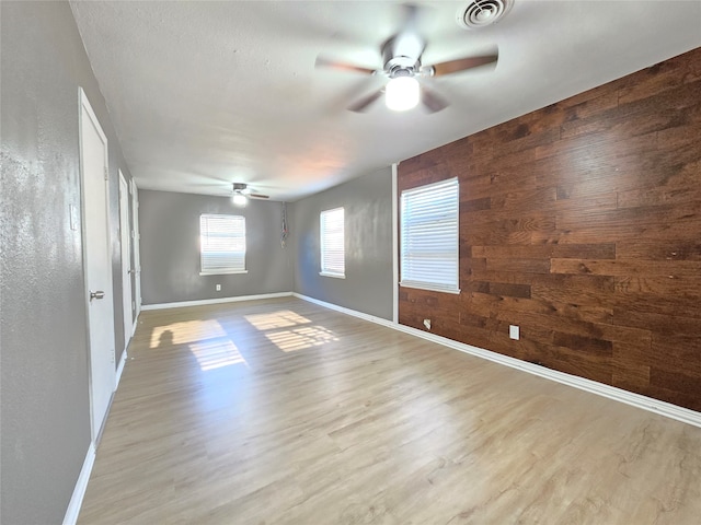 unfurnished room featuring ceiling fan, wood walls, and light hardwood / wood-style flooring