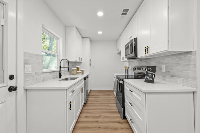 kitchen with stainless steel appliances, sink, backsplash, white cabinetry, and light hardwood / wood-style flooring