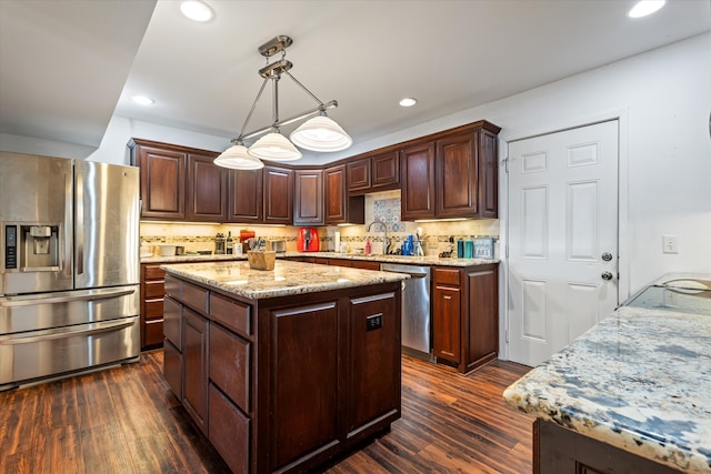 kitchen with appliances with stainless steel finishes, dark hardwood / wood-style flooring, decorative light fixtures, and a kitchen island