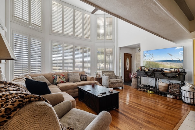 living room featuring a textured ceiling, beamed ceiling, wood-type flooring, and a high ceiling